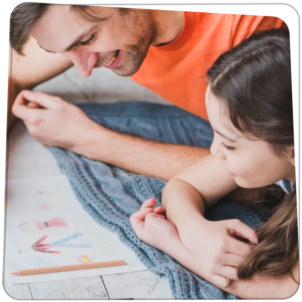 Apa és kislánya közösen nézik a gyerekrajzokat az asztalon.