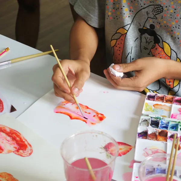 Gyermek fest vízfestékkel az asztalon, saját rajzát készítve a Rajzkönyvhöz.